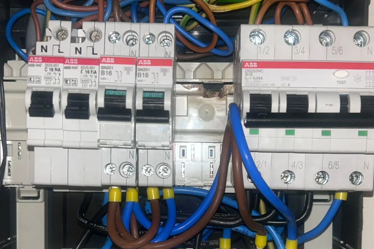 Praktijkfoto: overzicht van een groepenkast met installatieautomaten, aardlekschakelaars en warmteschade aan de aansluitrail